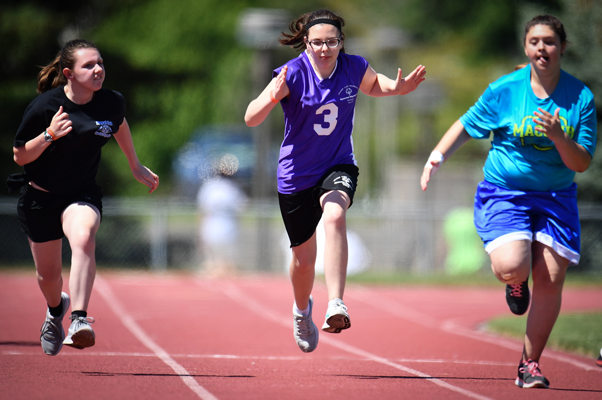 Three female athletes run the 100 meter dash.