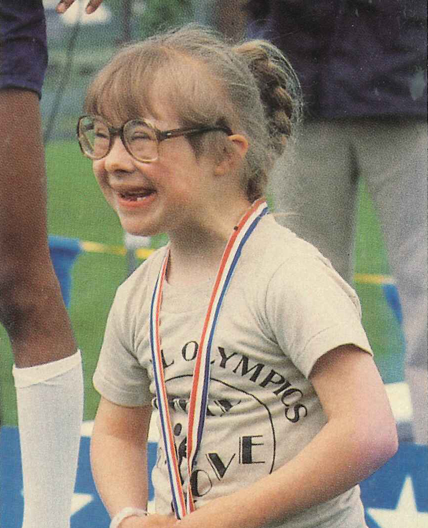 A young Special Olympics Michigan athlete smiles with a medal around her neck.