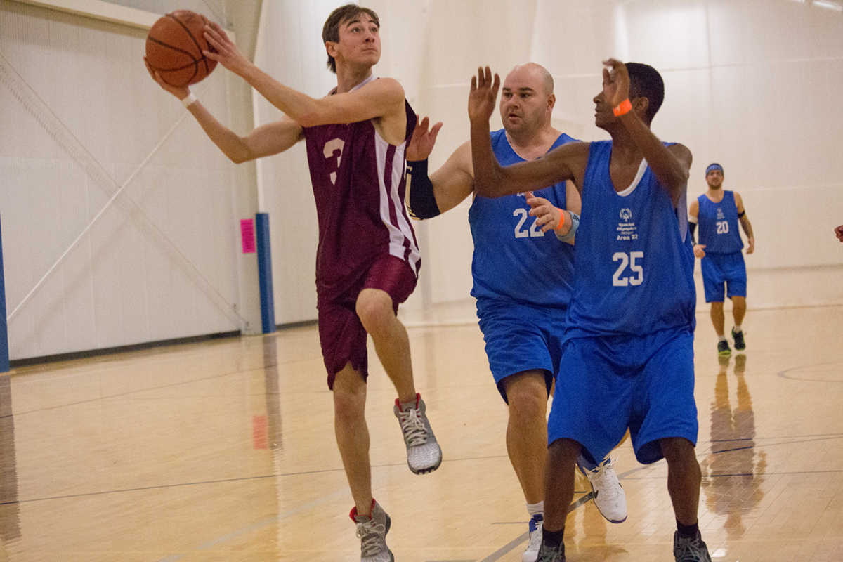A basketball player drives to the hoop against two defenders.
