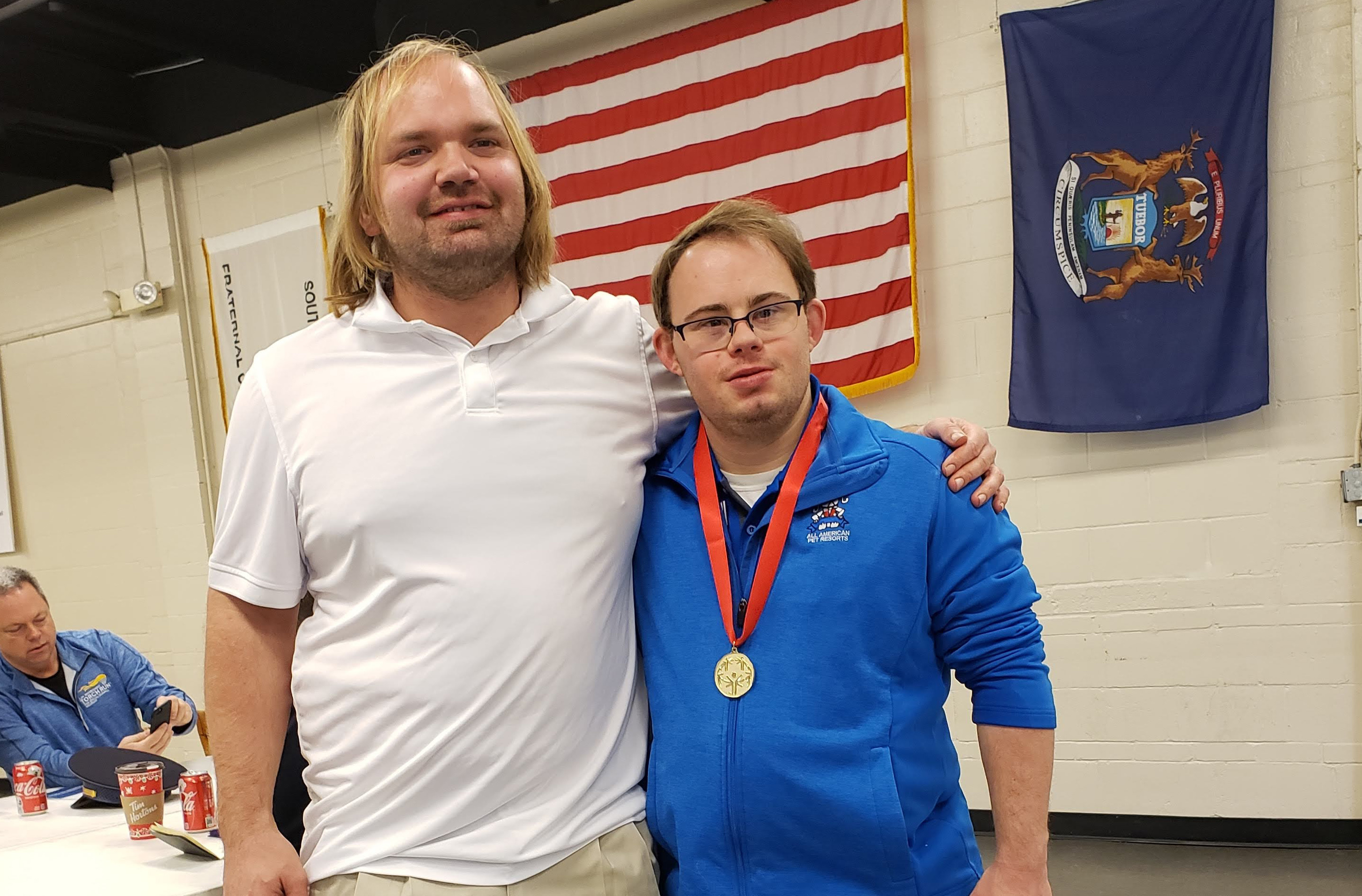 Two SOMI athletes pose for a photo together with an American flag in the background.
