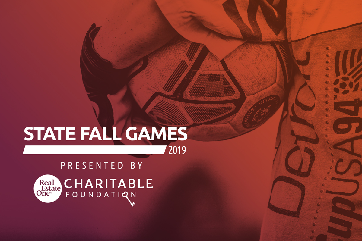 Closeup of a soccer ball being held by an athlete with the words State Fall Games presented by Real Estate One Charitable Foundation