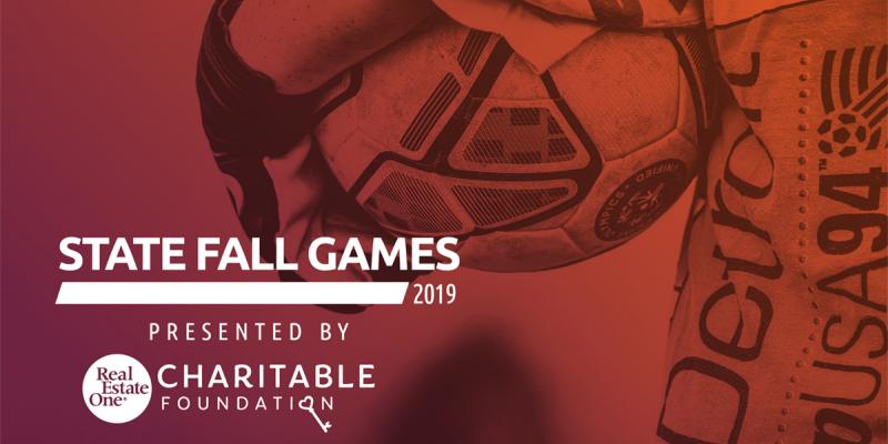 Closeup of a soccer ball being held by an athlete with the words State Fall Games presented by Real Estate One Charitable Foundation